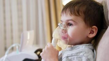 Boy using nebulizer for asthma. Child sits calmly while using a nebulizer, receiving respiratory treatment in a cozy room setting. video