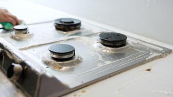 Scrubbing stove with dish soap. A person is scrubbing a dirty stove top with a green sponge, using soapy water to remove grease and grime. video