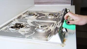 Cleaning a stove top after cooking. A person cleans a greasy stove top in a kitchen using a green cloth to remove residue and dirt. video