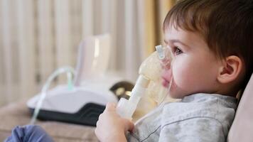 Child using nebulizer at home for health. A young child sits on a couch using a nebulizer for respiratory treatment at home in a cozy living room setting. video
