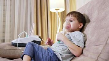 Child using nebulizer at home. A young boy sits on a couch, using a nebulizer to manage his respiratory condition while relaxing at home. video
