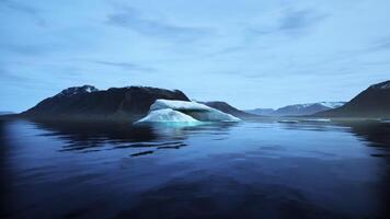 Majestic iceberg floating in calm waters with distant mountains at twilight video