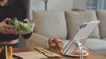 A woman is holding a salad in front of a tablet video