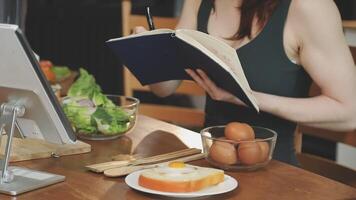 A woman is writing in a notebook while eating an egg and a bowl of vegetables video