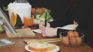 A woman writing on a piece of paper while sitting at a table with food video