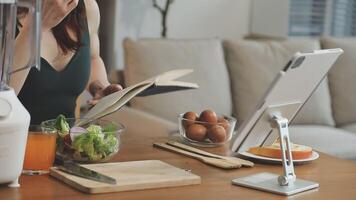 A woman is reading a book while sitting at a table with a blender and a cup of juice video