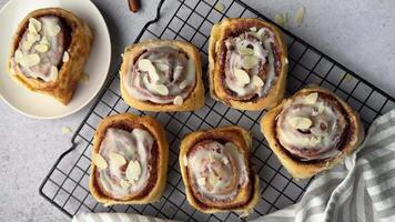 Delicious cinnamon rolls with icing and almond flakes on cooling rack video