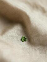 Natural linen fabric background with delicate texture and green clover accent photo