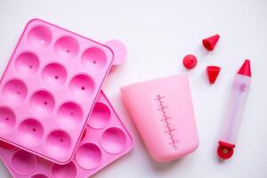 Pink baking utensils set with silicone molds and measuring cup on white background photo