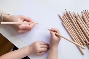 Child and adult drawing together with colored pencils on white paper photo