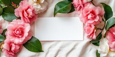 Elegant blank white card surrounded by fresh pink flowers on soft fabric background photo