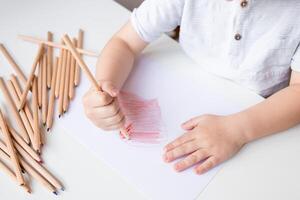 Child drawing with colored pencils on white paper photo