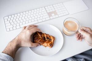 Caucasian male adult enjoying coffee and pastry at office desk with keyboard photo