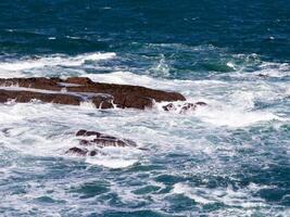 Waves crashing on rocky seashore under clear blue sky photo