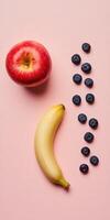 Minimalistic flat lay with bright red apple, banana, and blueberries on pink background for modern design photo