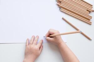 Child drawing with pencils on white paper surface photo