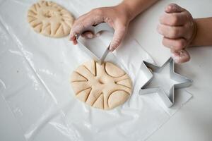 Child hands creating star shaped cookies on plastic sheet with cookie cutter photo