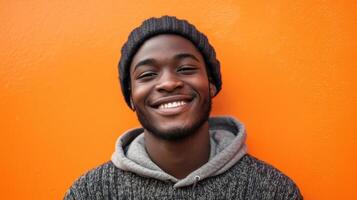 A young man is smiling while standing in front of an orange wall photo