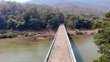bridge over river in the forest, view of a rural bridge crossing a river in a mountainous landscape during the dry season. The bridge connects two forested areas with lush greenery video