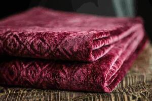 Folded Burgundy Velvet Fabric with Decorative Pattern on Textured Surface in Soft Light Close-Up photo
