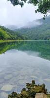 Serene Mountain Lake With Crystal Clear Water And Lush Green Forest Reflections Under Foggy Sky photo