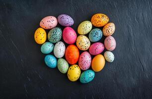 Heart Shaped Arrangement of Vibrantly Colored Speckled Easter Eggs on Dark Stone Background photo