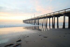 Rustic Ocean Pier Extending Over Calm Waves at Sunrise with Reflections on Sandy Beach Waterscape photo