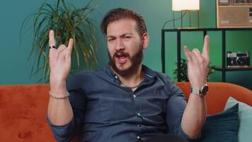 Overjoyed young lebanese man showing rock n roll gesture, cool sign dancing rejoicing in success video