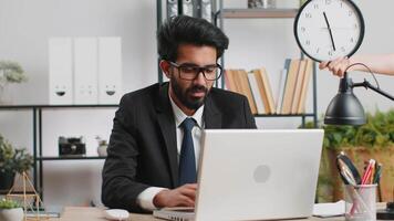 Indian businessman with anxiety checking time on clock, running late to work being in delay deadline video