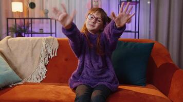 Smiling toddler girl friendly at camera, waving hands gesturing hello, hi, greeting at home on sofa video