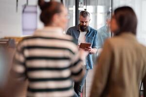 Senior bearded businessman, IT professional, trader, and crypto investor using a digital tablet in a modern coworking space. Tech-savvy professional working in an open office startup environment photo