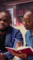 Mature people overseeing schedule and planning activities at coffee table, working on time management with online tools. Couple utilizing a notebooks and taking handwritten notes. Camera B. video