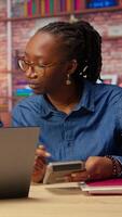 African american man and woman review earnings and revenue reports in their apartment, using calculator and laptop to ensure accurate accounting and financial planning for the tax season. Camera A. video