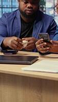 Young black couple sharing ear buds to listen to webinar on smartphone, working together on their freelancing tasks at home. Man and woman discussing about a work project. Camera A. video