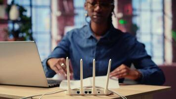 African american woman restarting her wireless router and checking network settings to resolve an internet error disrupting her daily tasks. Frustration due to signal loss. Camera B. video