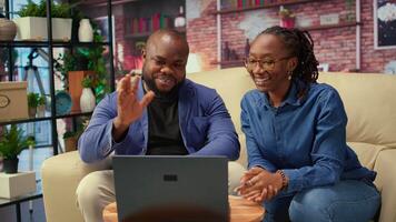 Black young couple attending an online call connection at home, sitting on the couch and talking to their friends. Man and woman waving on a conference, lifestyle. Camera A. video