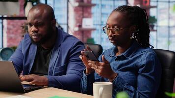African american people solving their daily work tasks at home office, using laptop and smartphone to ensure easy remote communication. Young couple with creativity. Camera B. video