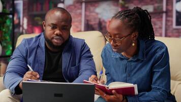 Black man and woman writing a report with information from notebook and archived files, improving networking skills and achieving career independence. Freelancers solving tasks. Camera B. video