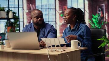 African American couple at home office troubleshooting their Wi Fi modem and discussing solutions to fix a weak connection affecting their remote work productivity. Router guide files. Camera B. video
