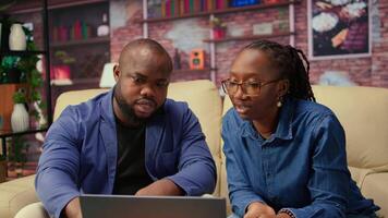 African american people on the sofa discussing a freelance strategy, researching marketing trends and online data from analytics tools to create a growth report. Remote efficiency. Camera A. video
