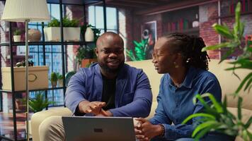 Black couple in living room discusses creative ideas for an online business, using modern technology to research trends and improve efficiency. Motivation and support for success. Camera A. video