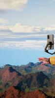 Vertical Influencer recording a in the mountains sharing his outdoor journey with his audience. Male trekker always connected with a smartphone placed on a stabilizing tripod. Camera B. video