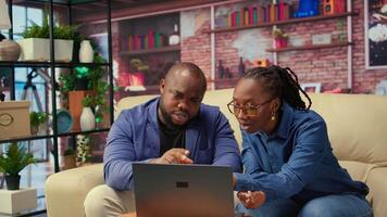 Freelancer couple doing research by reading articles and data driven papers at home, collecting information for a new project. People multitasking and studying online reports on sofa. Camera A. video