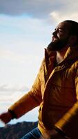 Vertical Victorious adventurer celebrates on top of a mountain and dancing, embracing the peaceful solitude and breathtaking views. Nature lover enjoys majestic wilderness and ambition. Camera B. video