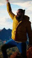 Vertical Proud explorer reaches the top of the mountain feeling satisfied and pleased with his accomplishment, scenic background of mountains and sky. Self improvement and new horizons. Camera A. video