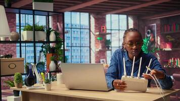 Black woman at home examines the modem and troubleshooting guide book, struggling to fix Wi Fi router and restore her internet connection for remote freelance tasks. Signal loss. Camera A. video