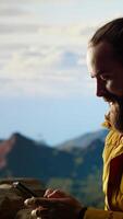 Vertical Trekker enjoys a quiet moment in the mountains scrolling phone app, where the high altitude air and breathtaking view encourage mindfulness. Relaxation and self improvement. Camera B. video