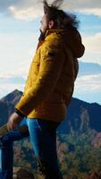 Vertical Happy adventurer embraces the thrill of standing at the top of the mountain, feeling the power of accomplishment. Awe inspiring mountain range with peaceful sky and vast wilderness. Camera A. video