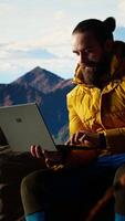 Vertical Nature lover workaholic always connected to the internet and scrolling on laptop, enjoying strong signal on a mountain top with a breathtaking landscape. Uninterrupted work. Camera B. video