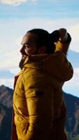 Vertical Proud explorer reaches the top of the mountain feeling satisfied and pleased with his accomplishment, scenic background of mountains and sky. Self improvement and new horizons. Camera B. video